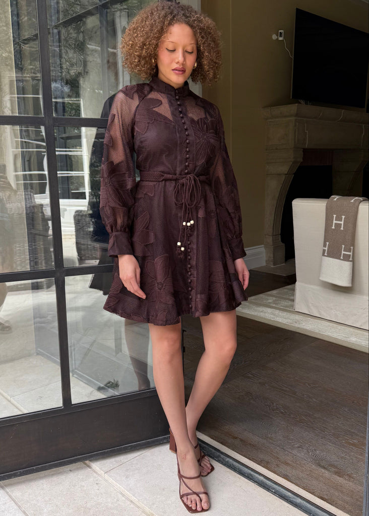 Woman in a brown dress standing in a doorway with a view of a living room.