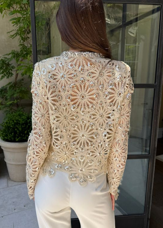 Person wearing a beige lace top with floral patterns and embellishments.