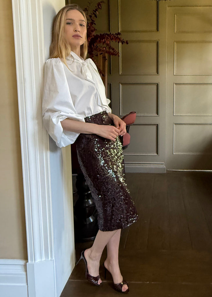 Woman in a white blouse and sequin skirt standing in a doorway.