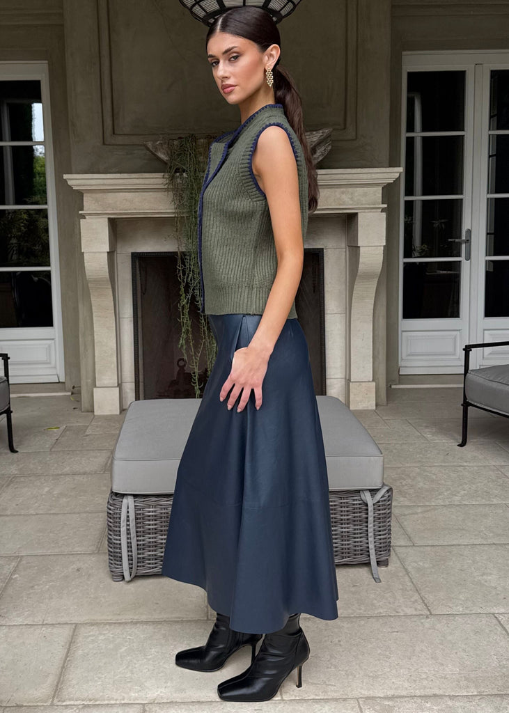 Woman in a green sleeveless top and blue skirt standing on a patio with decorative elements.