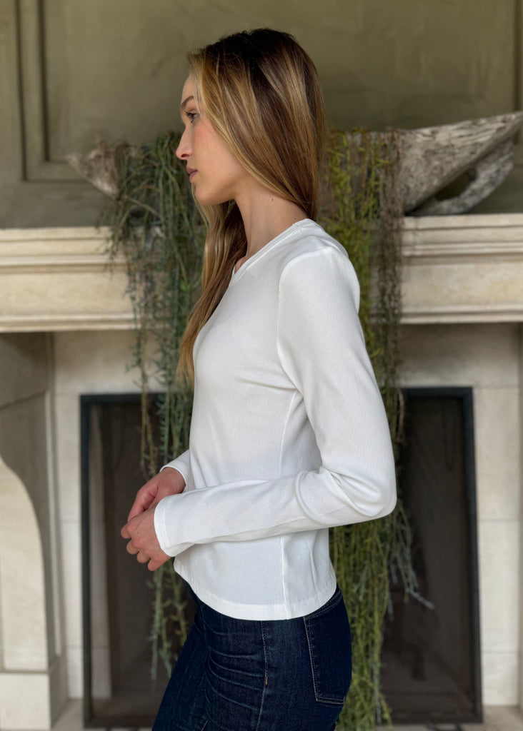 Woman wearing a white long-sleeve shirt standing in front of a fireplace.