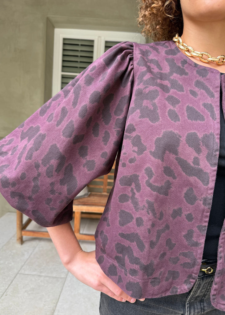 Person wearing a purple leopard print jacket with a neutral background