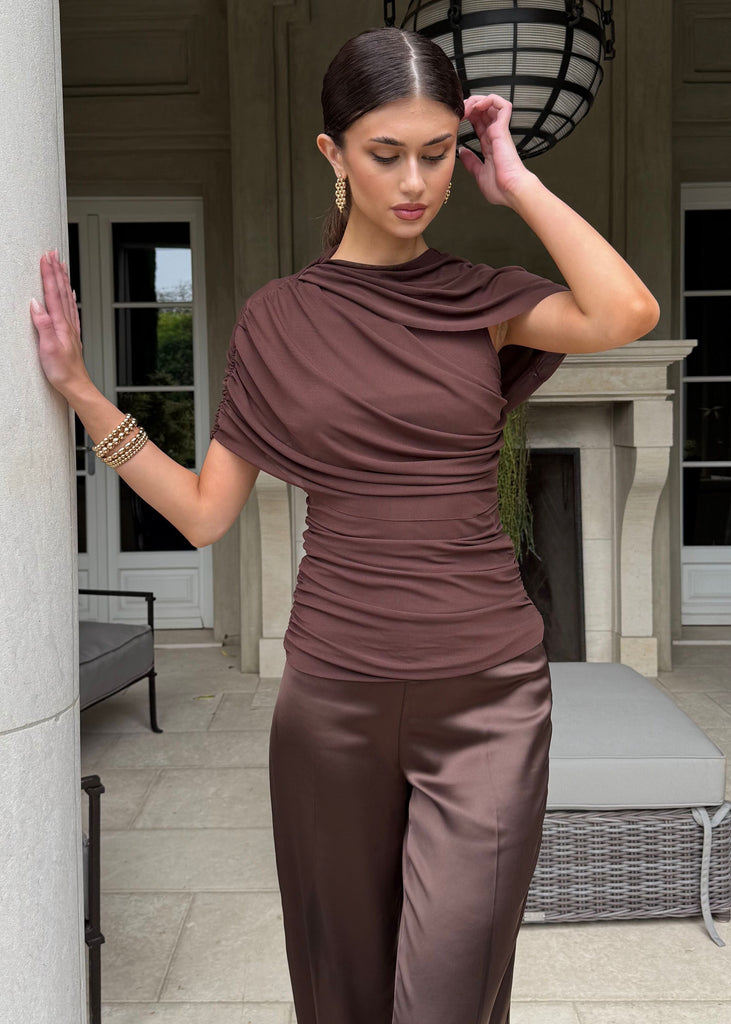 Woman in a brown outfit standing in a stylish outdoor setting.