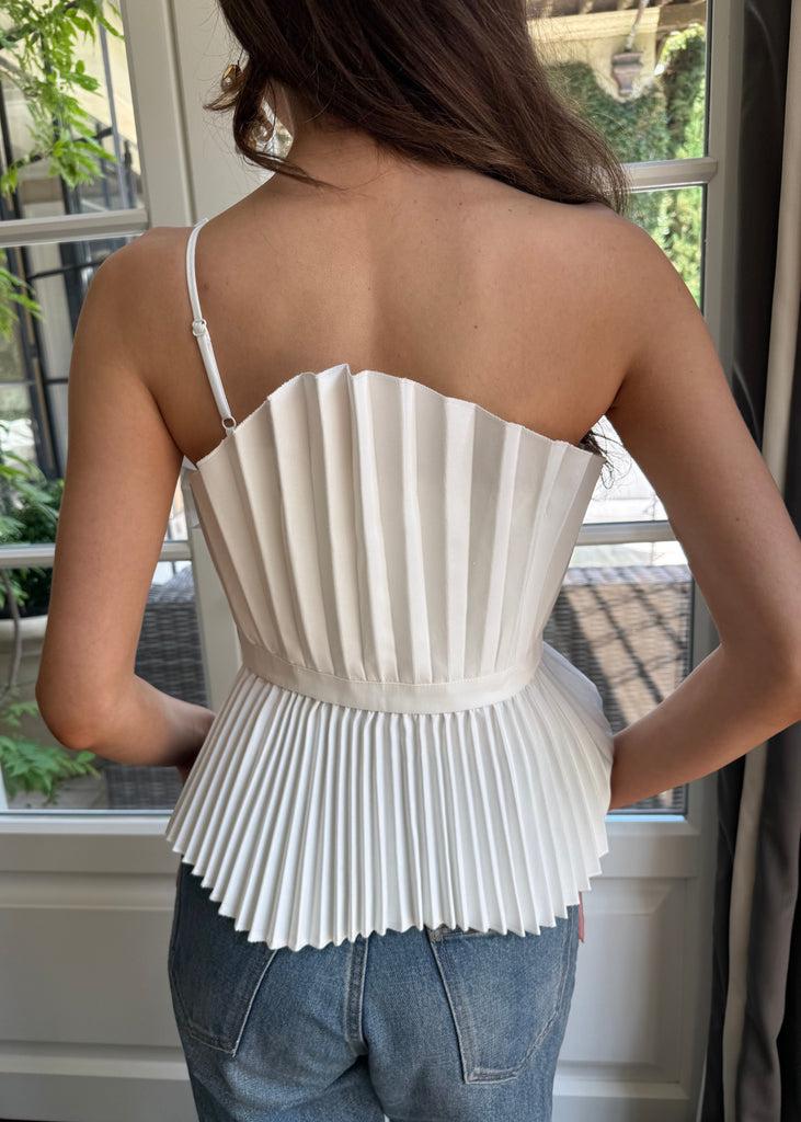 Woman wearing a white pleated top with thin straps, standing indoors.