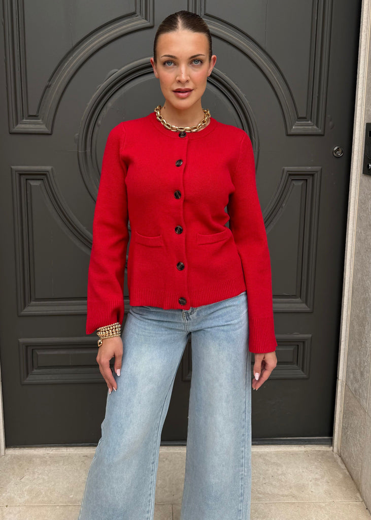 Woman wearing a red jacket and light blue jeans standing in front of a black door.