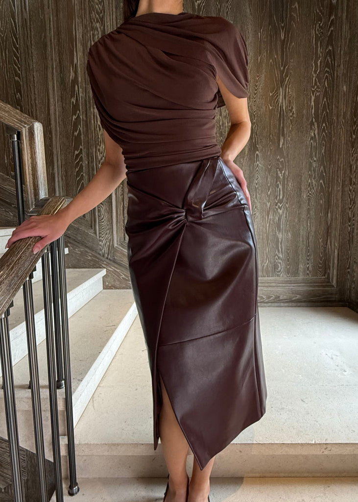 Woman in a brown dress standing on a staircase in a wooden-paneled room.