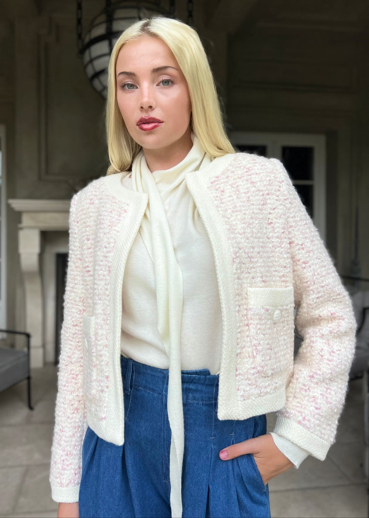 Woman wearing a white textured cardigan, white blouse, and blue pants outdoors.