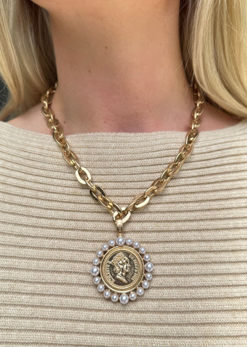 Gold chain necklace with a pendant featuring a face design and pearls on a beige sweater.