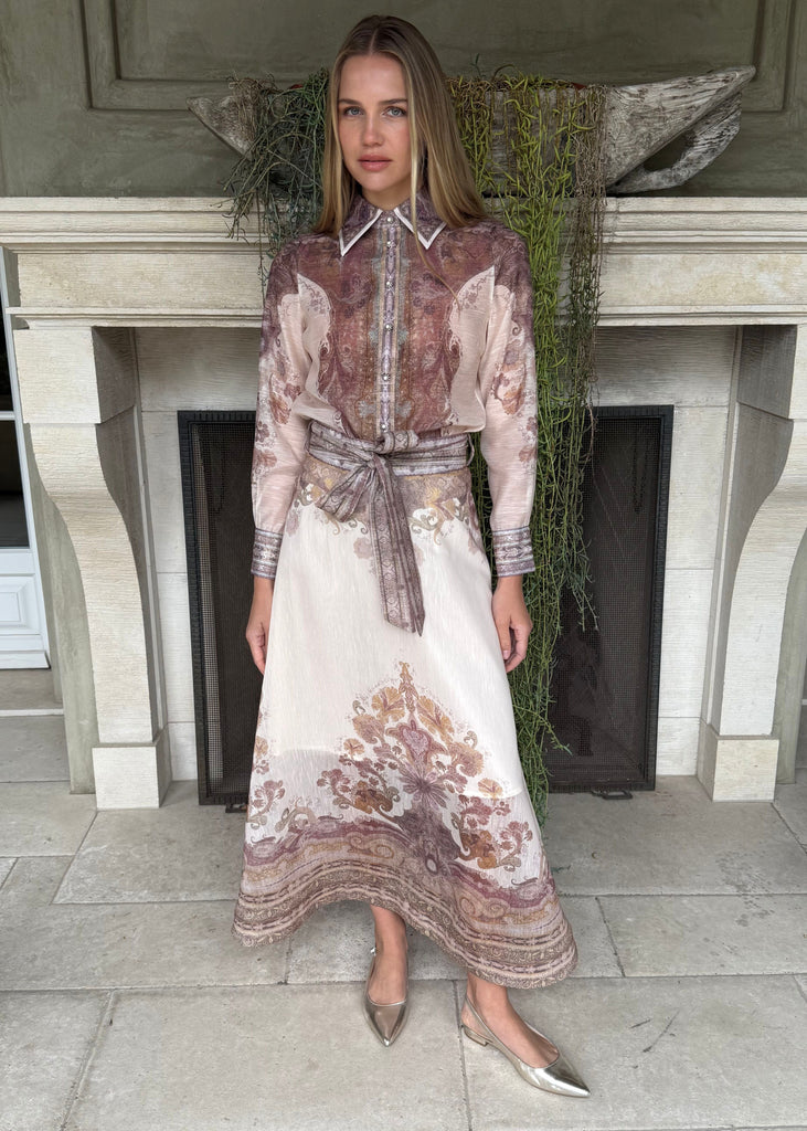 Woman in a floral dress standing in front of a fireplace.