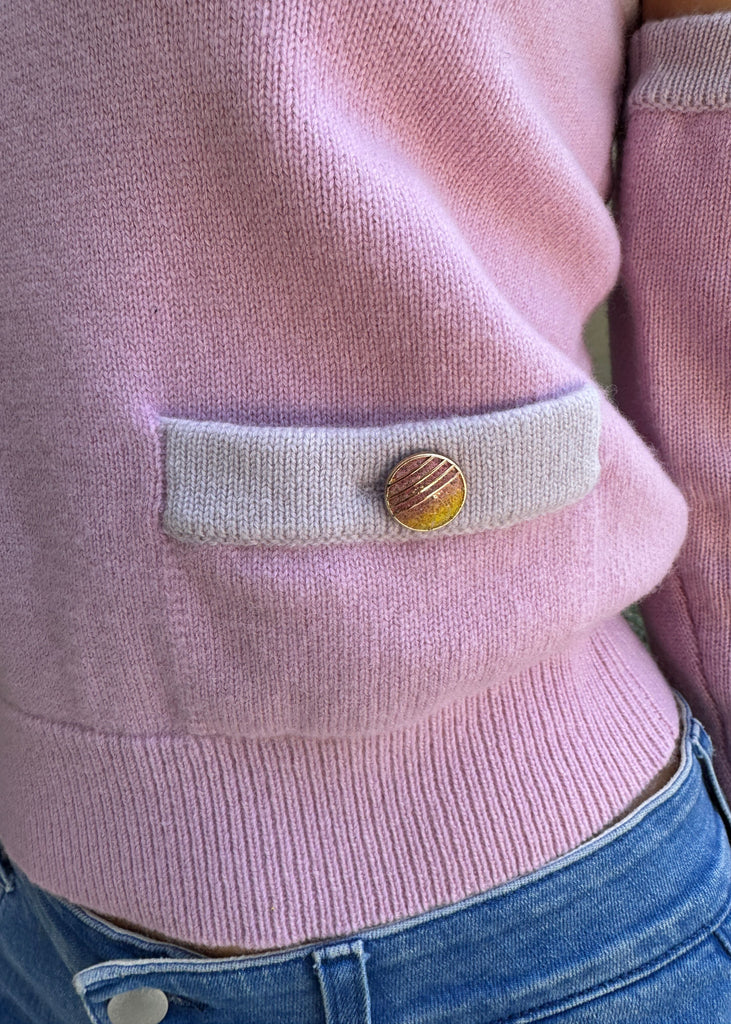 Close-up of a pink sweater with a button on a person wearing blue jeans.