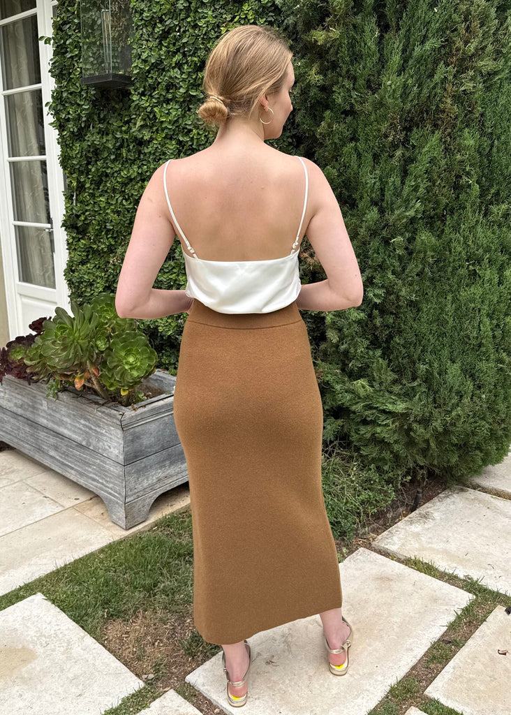 Woman in a white top and brown skirt standing in a garden setting.