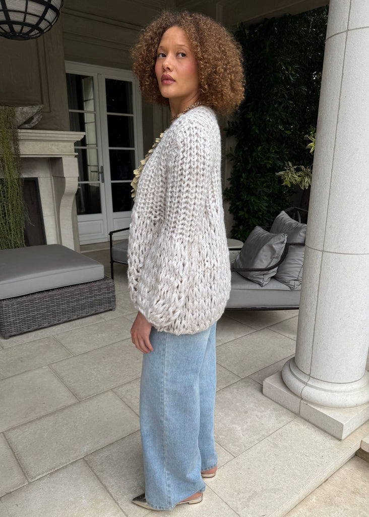 Woman wearing a textured white sweater and light blue jeans standing on a patio.