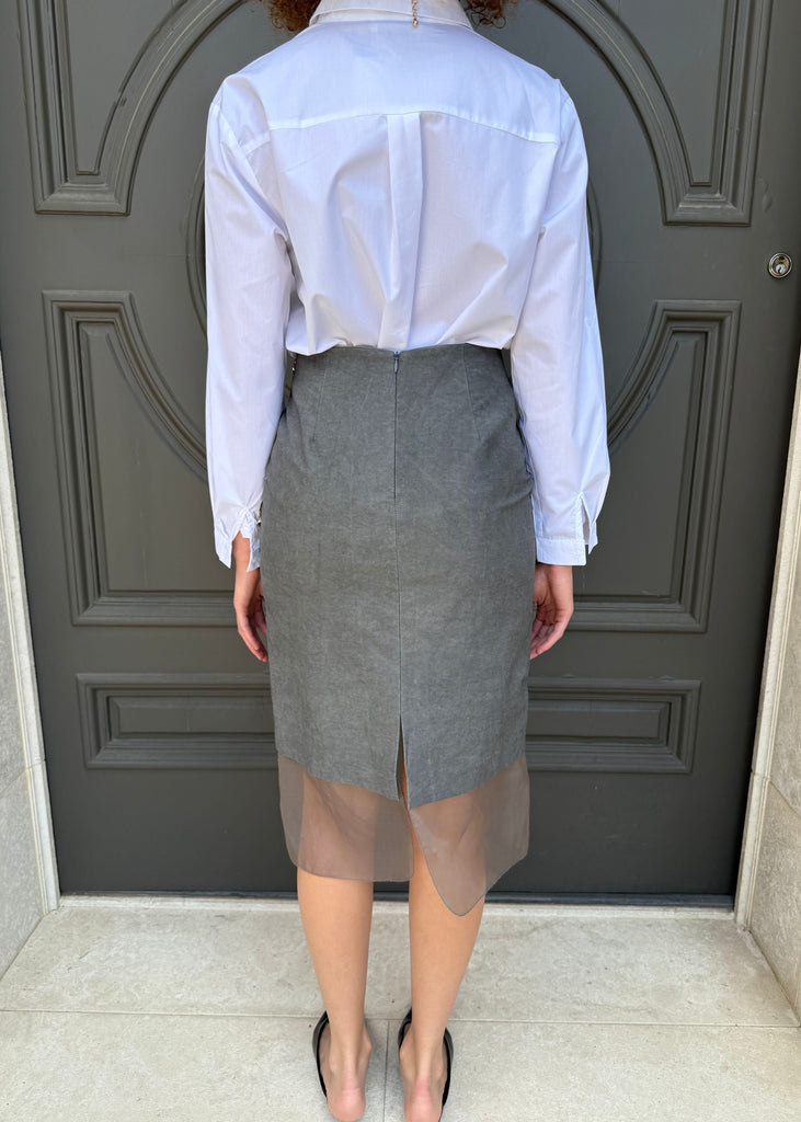 Person wearing a white shirt and gray skirt standing in front of a gray door.