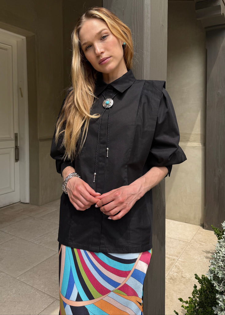 Woman wearing a black shirt with a colorful skirt standing outdoors.