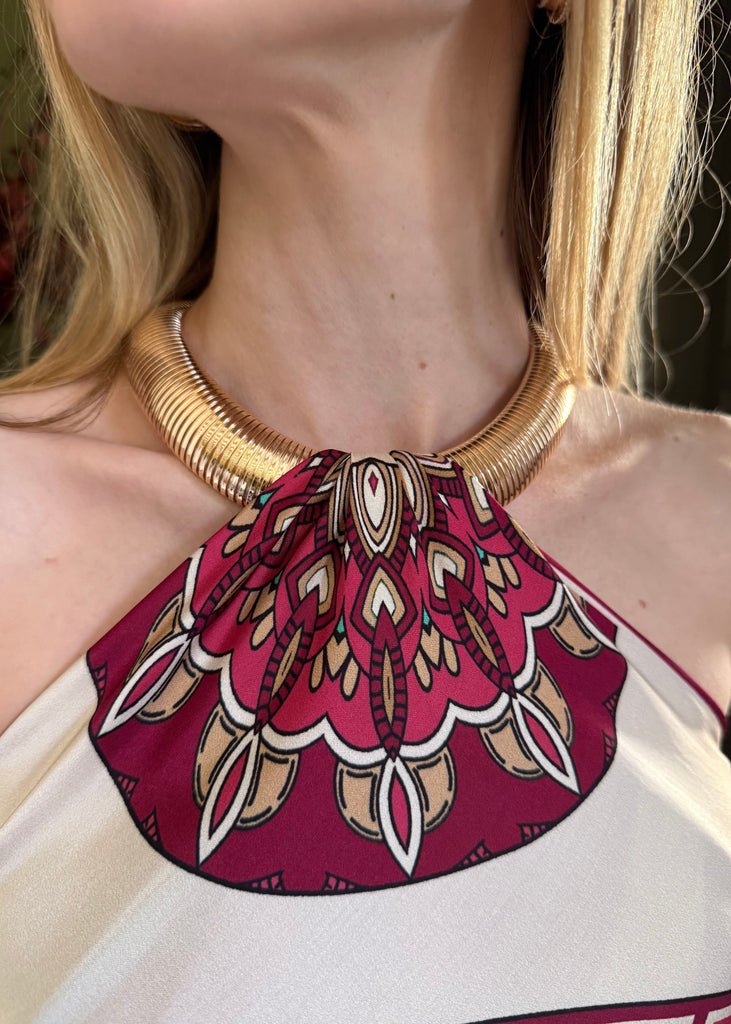 Close-up of a woman wearing a gold necklace and a dress with a red and white pattern.