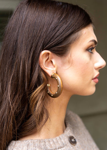 Close-up of a woman wearing gold hoop earrings with a blurred background
