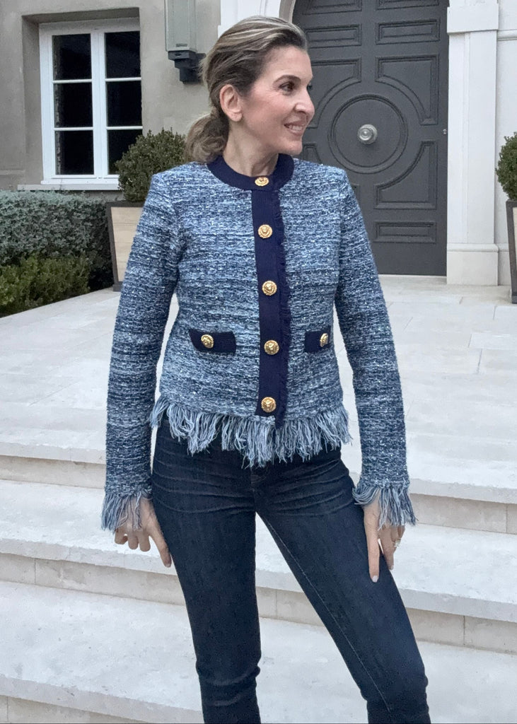 Woman in a blue textured jacket standing in front of a building with a decorative entrance.