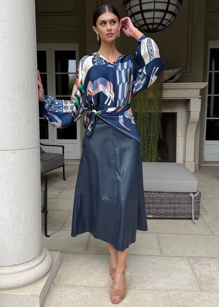 Woman in a blue dress with a patterned top standing on a patio.