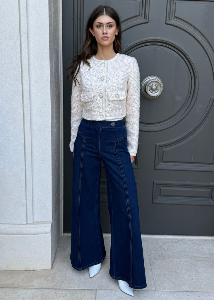 Woman in a white sweater and navy pants standing in front of a gray door.
