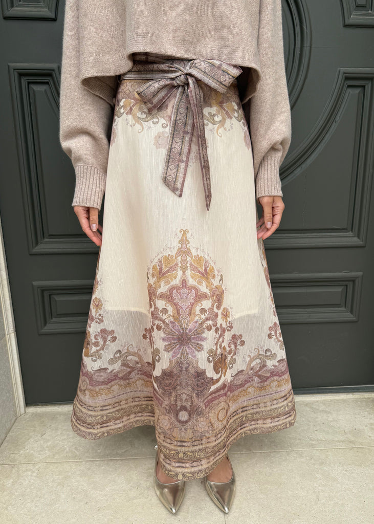 Person wearing a patterned skirt and beige sweater in front of a dark gray door.