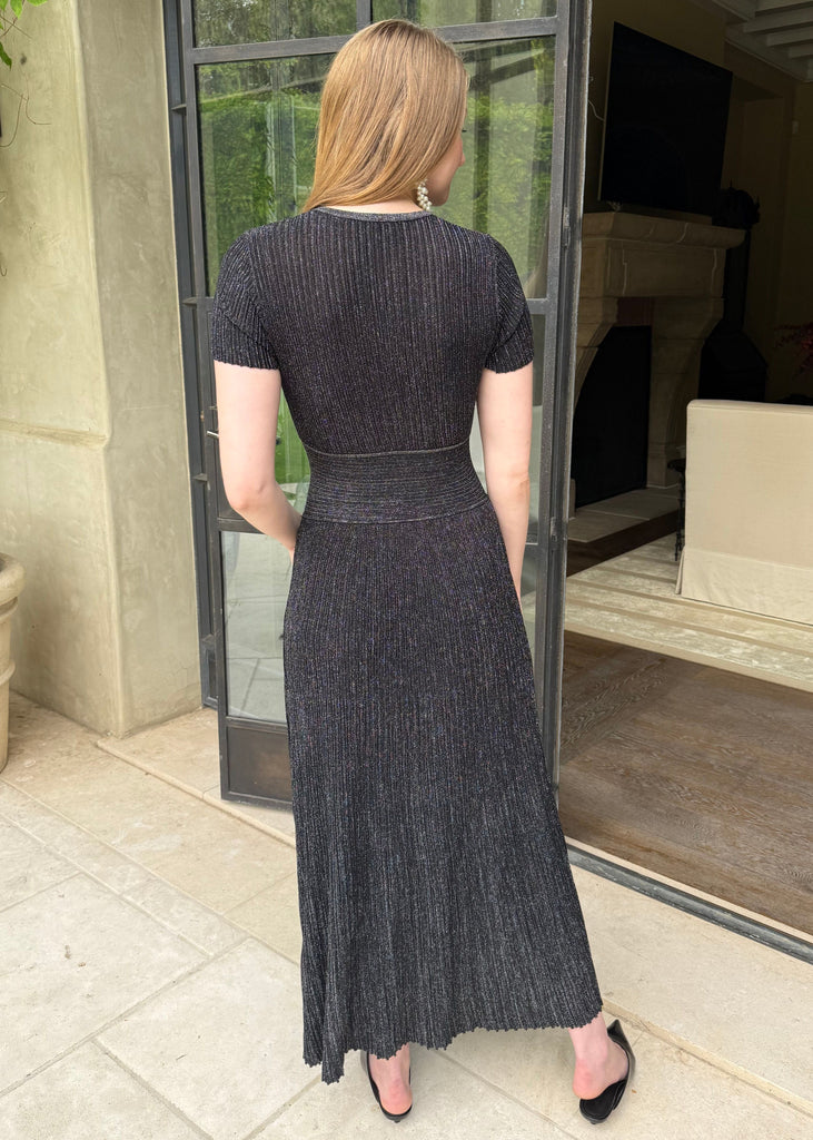 Woman in a black dress standing in a room with a large window.