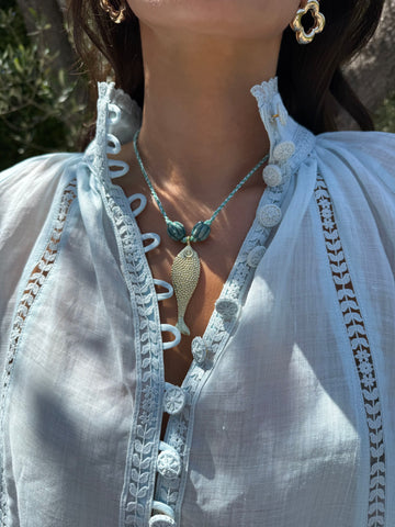 Close-up of a person wearing a light blue embroidered top and a necklace with a pendant.