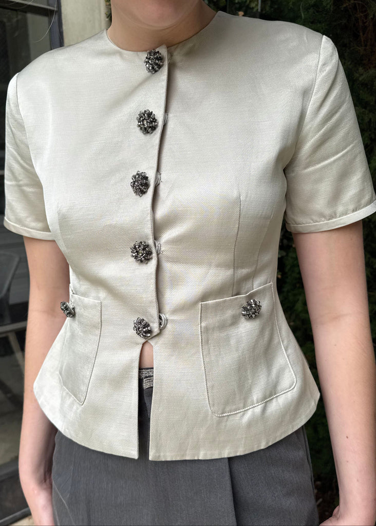 Person wearing a beige short-sleeve blouse with floral buttons outdoors.