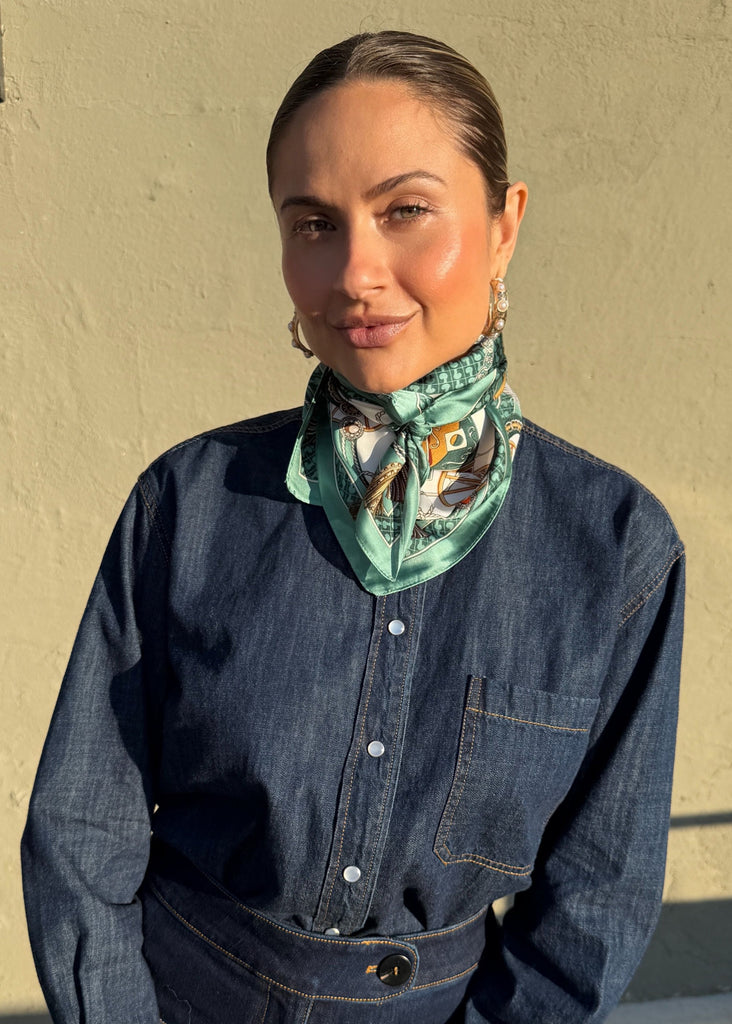 Person wearing a denim jacket and patterned scarf against a beige wall.