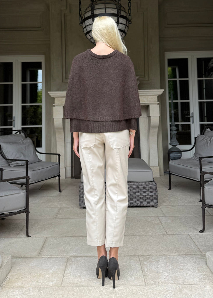 Person standing in a stylish outdoor setting with columns and furniture.