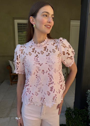 Woman wearing a pink lace blouse standing outdoors.