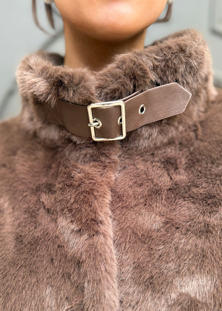Close-up of a brown fur coat with a leather strap and buckle.