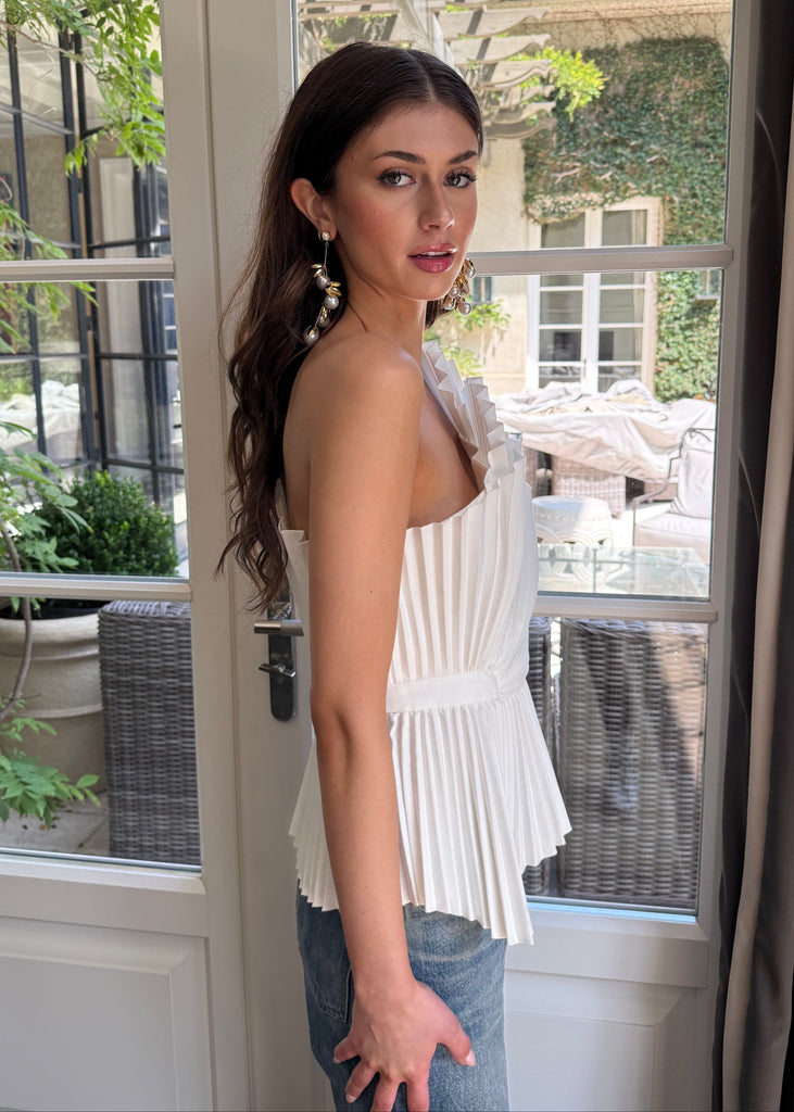 Woman standing in a room with a large window, wearing a white top and blue jeans.