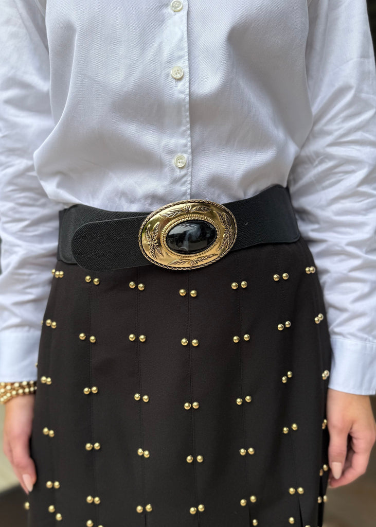 Person wearing a white shirt and black skirt with gold studs and a large belt buckle.