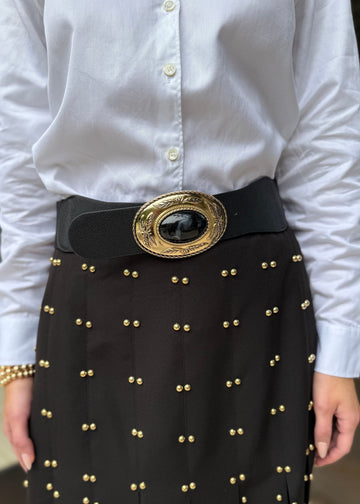 Person wearing a white shirt and black skirt with gold studs and a large belt buckle.