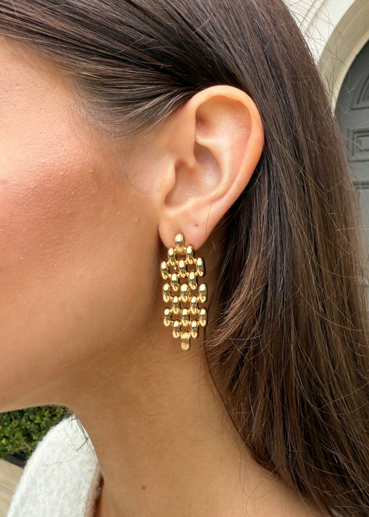 Gold chain earring worn by a person with a neutral background