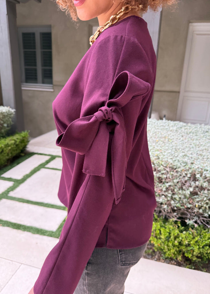 Person wearing a purple sweater with a bow detail outdoors.