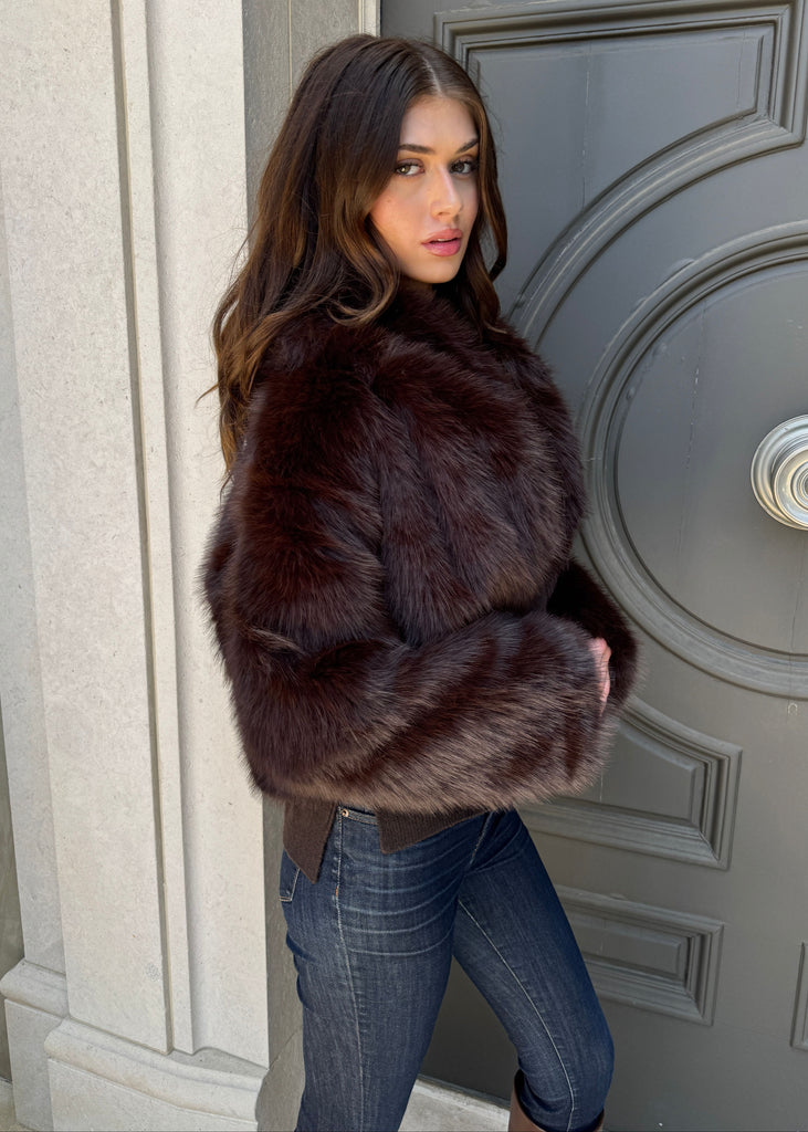 Woman wearing a fur coat standing in front of a door.