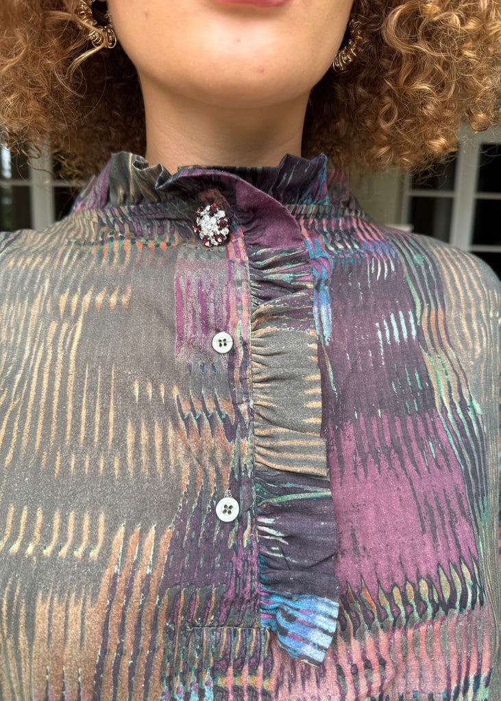 Close-up of a person wearing a patterned shirt with a decorative brooch.