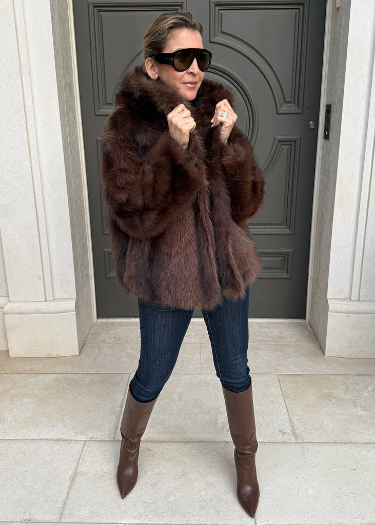 Person wearing a fur coat and sunglasses standing in front of a door.