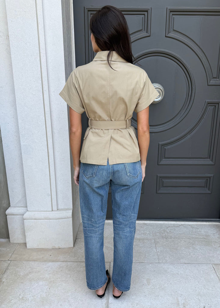 Person wearing a beige shirt and blue jeans standing in front of a dark gray door.