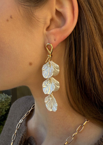 Close-up of a person wearing gold leaf-shaped earrings.
