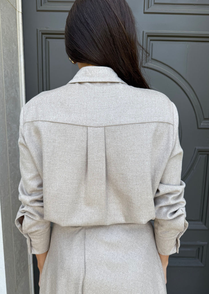 Person wearing a light gray coat standing in front of a dark gray door.