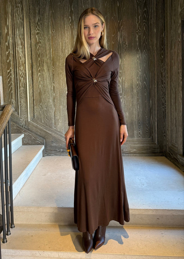 Woman in a brown dress standing in a room with wooden walls and a staircase.