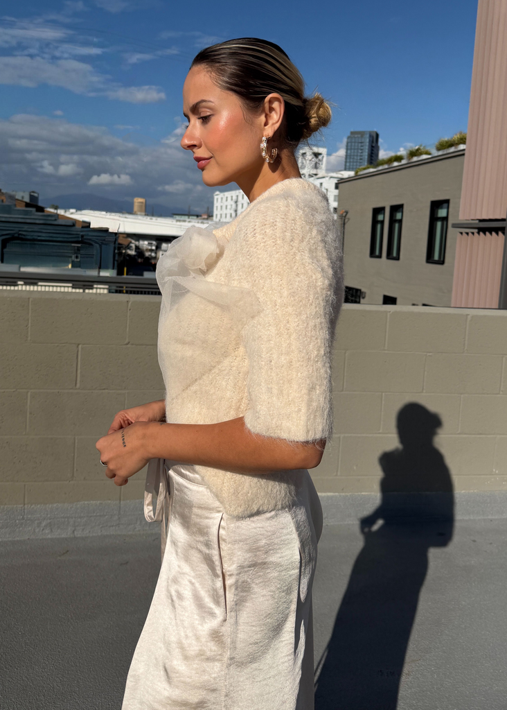 Woman in a white outfit standing on a rooftop with a cityscape background