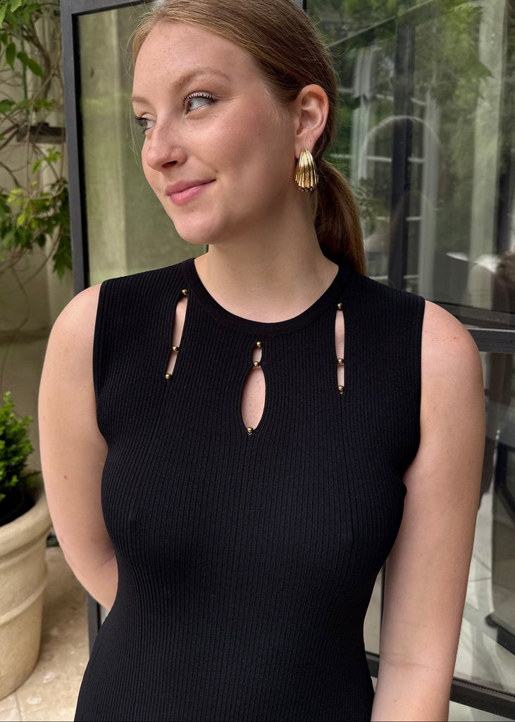 Woman wearing a black dress with cut-out details and gold earrings, standing outdoors.