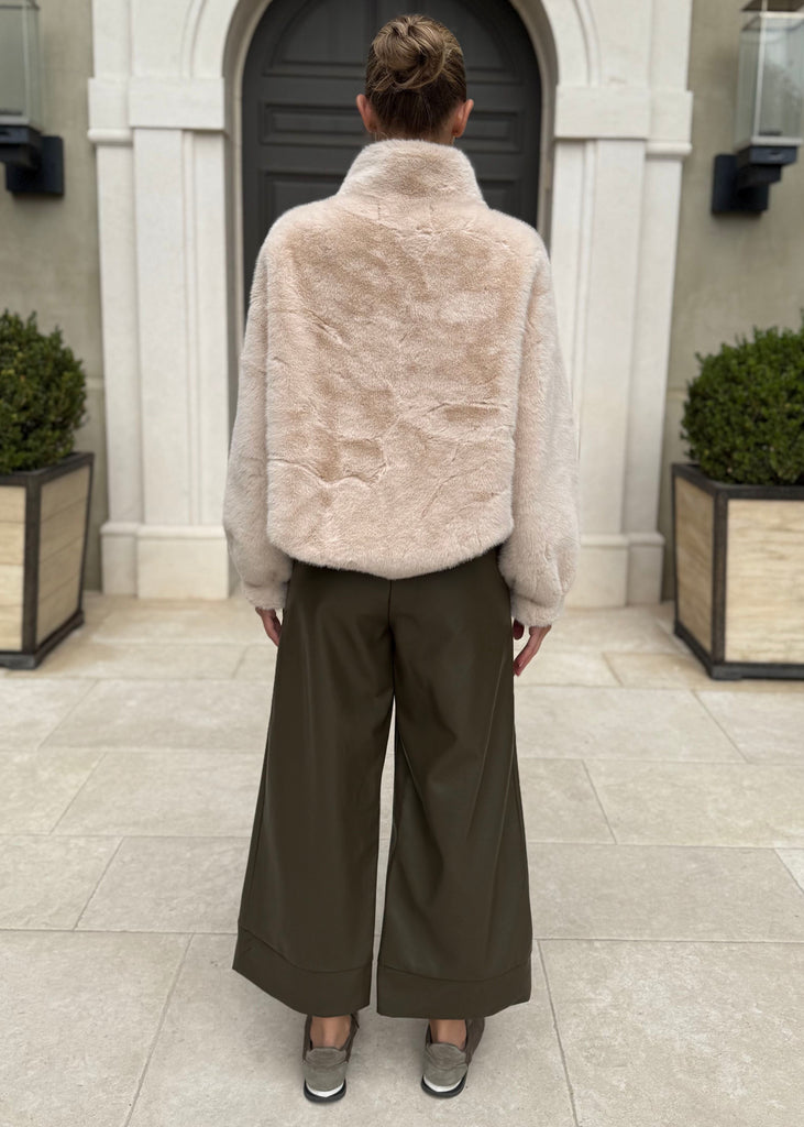 Person wearing a beige puffer jacket and dark pants standing in front of a building entrance.