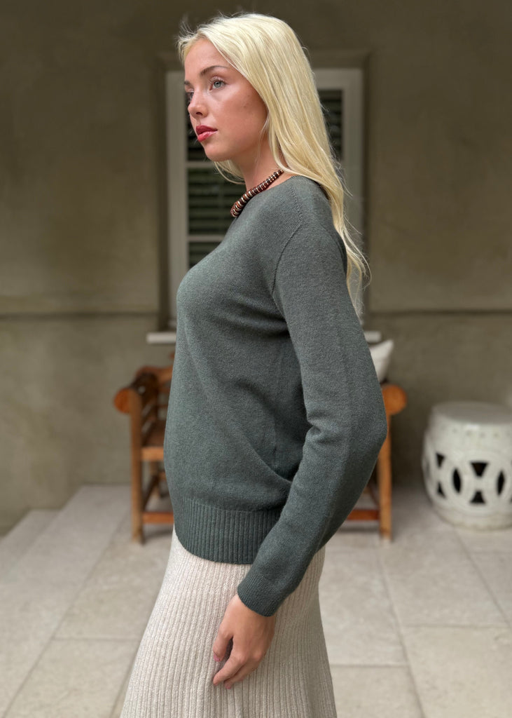 Woman wearing a green sweater and white skirt standing on a porch.