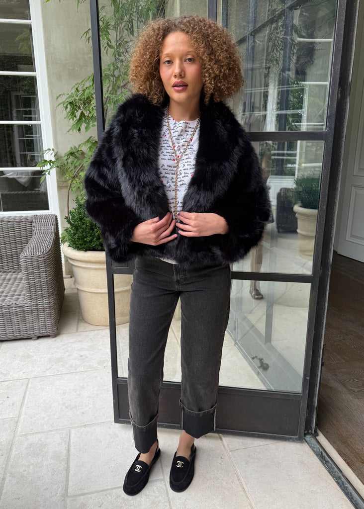 Person wearing a black fur coat standing in front of a glass door.