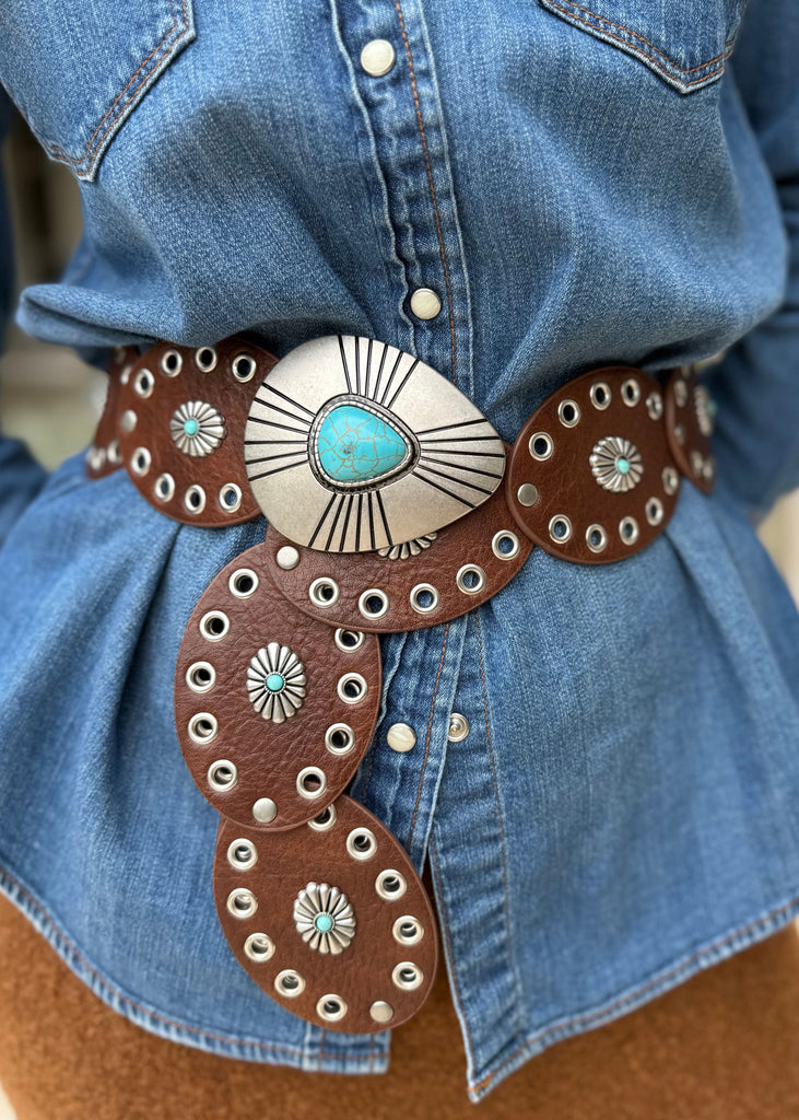 Person wearing a blue denim shirt with a decorative brown belt featuring turquoise stones.