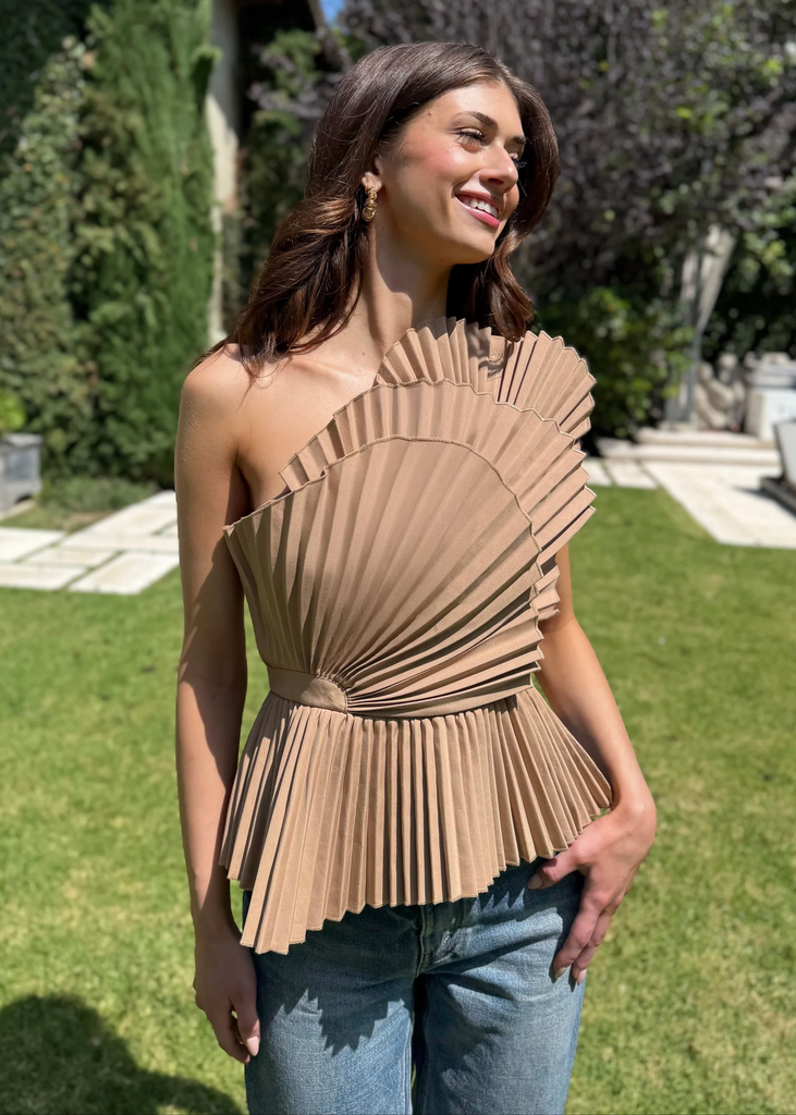 Woman wearing a beige pleated top outdoors on a sunny day